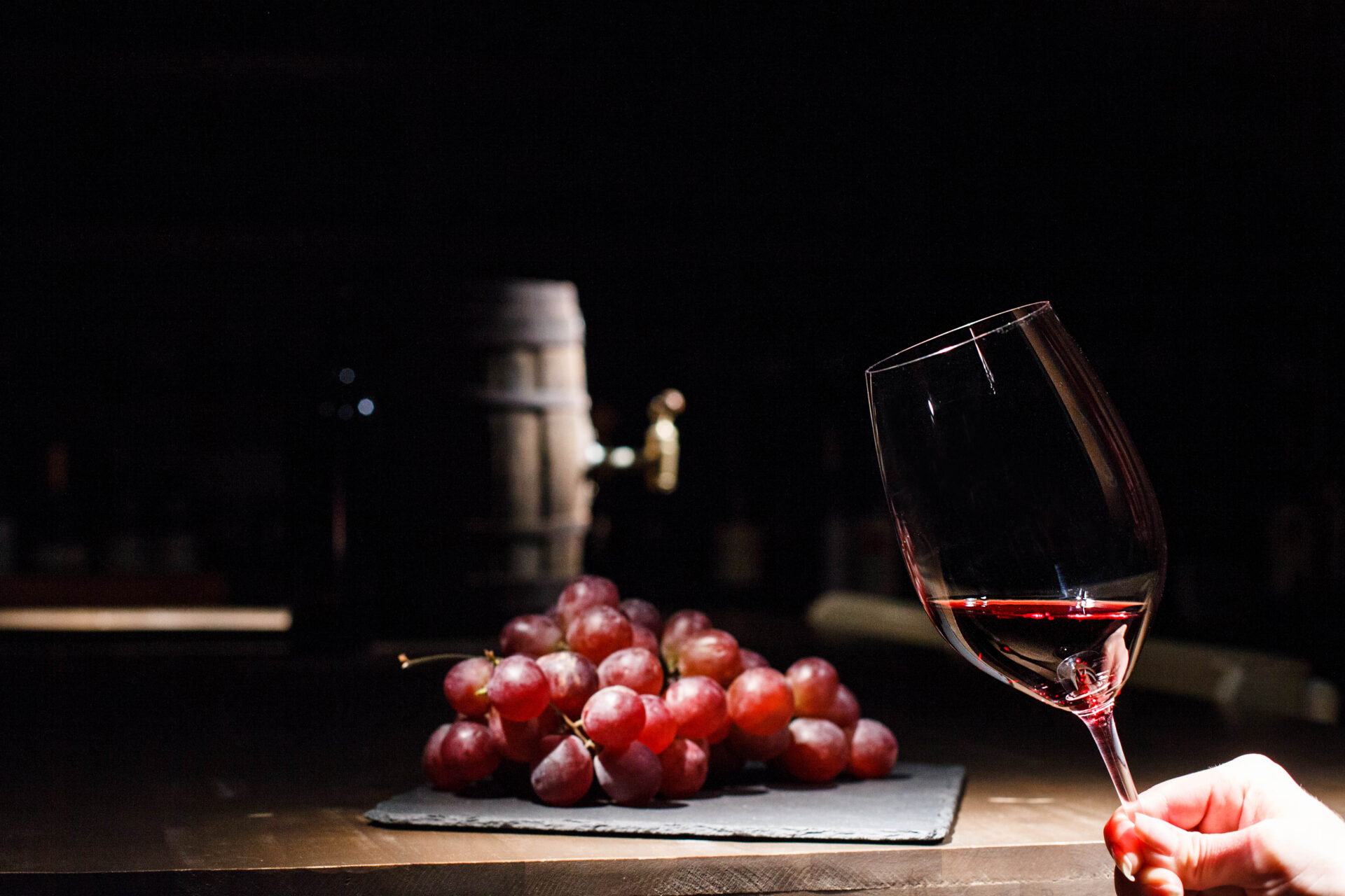 Woman holds glass of wine before bunch of grape lying on black plate